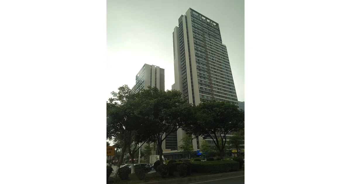 Edifícios altos com árvores, automóveis e calçada em primeiro plano.