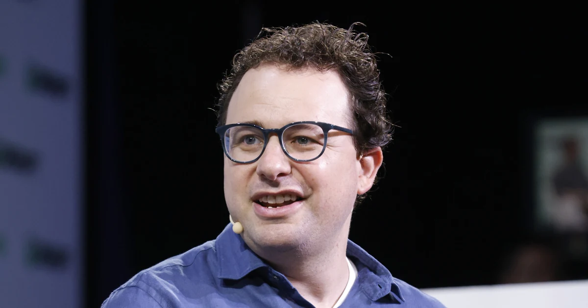 Dario Amodei no palco do TechCrunch Disrupt 2023, com óculos e camisa azul