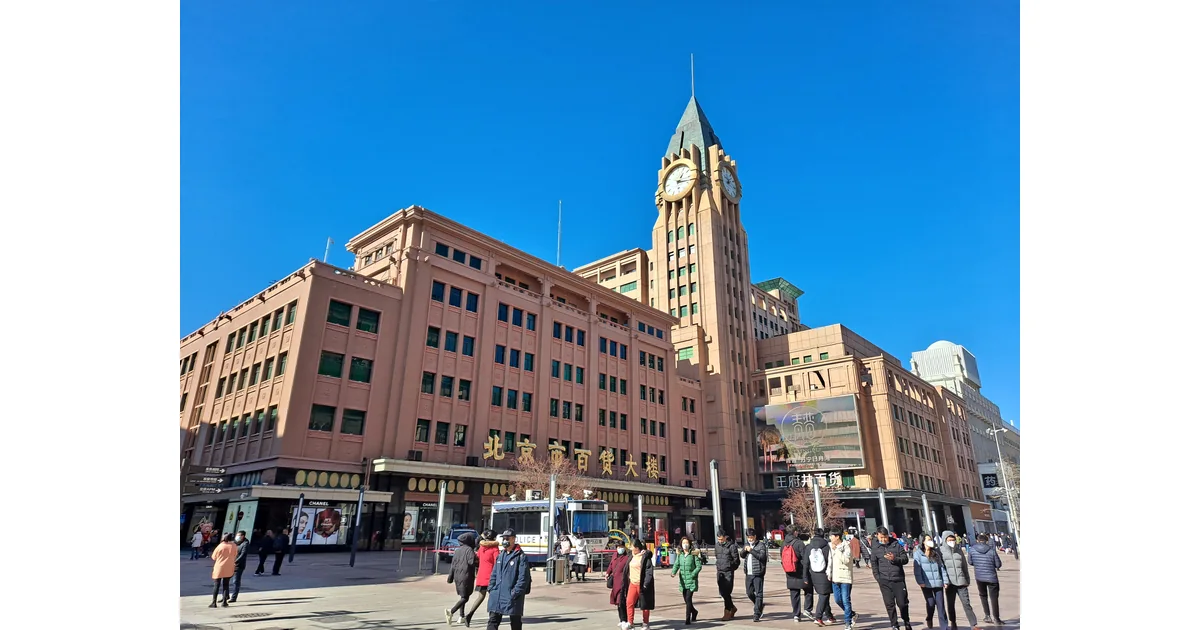 Fachada comercial com torre de relógio, letreiros e pedestres.