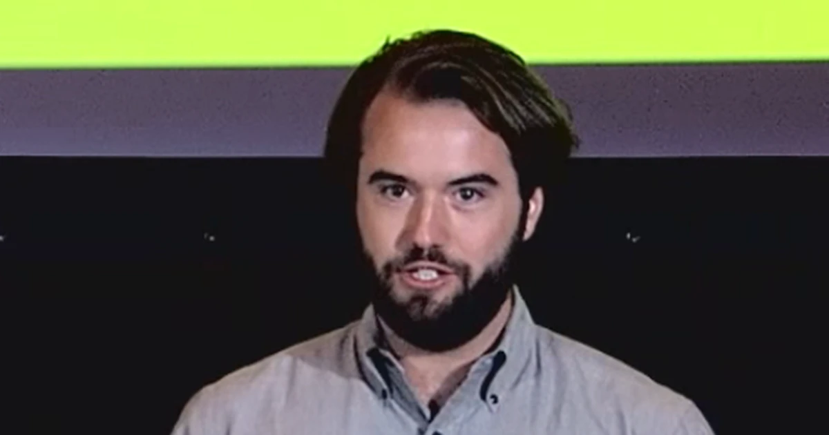 Chris Best de camisa cinza, falando durante uma apresentação em 2015