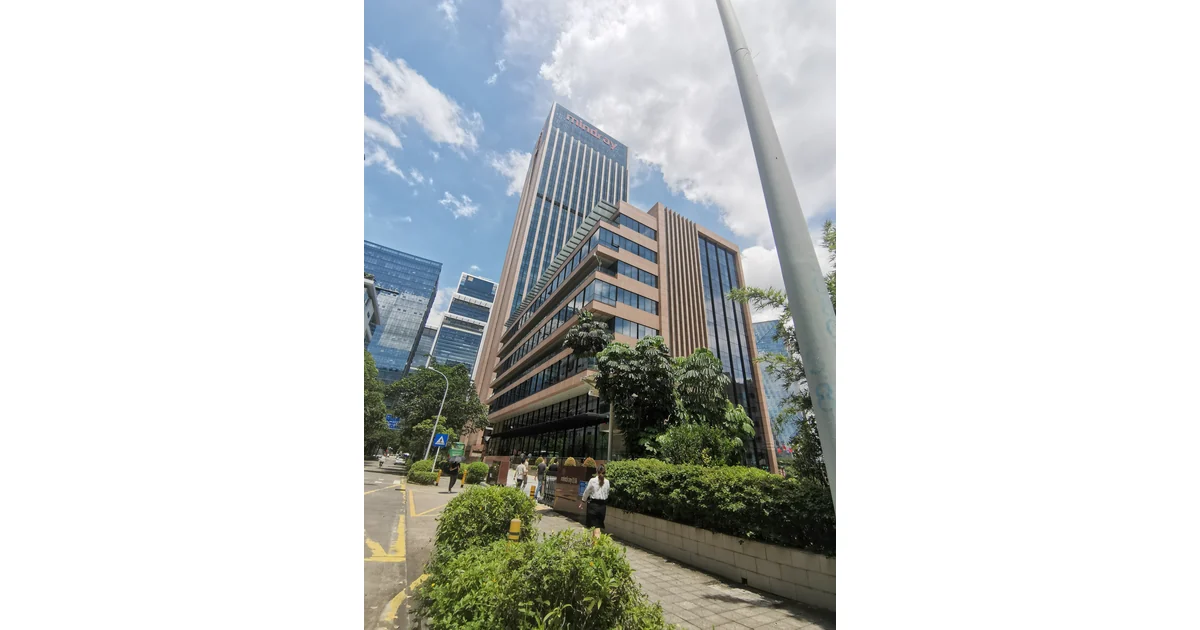 Edifício com fachadas de vidro, árvores e pedestres.