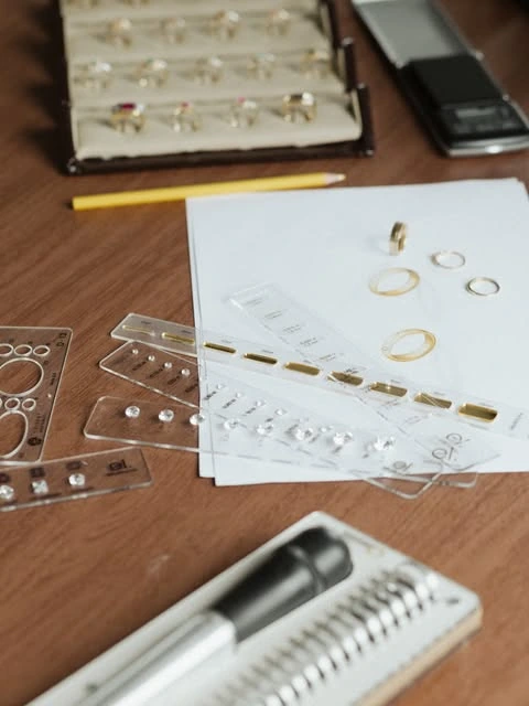 Joias, réguas e desenhos sobre uma mesa de trabalho.
