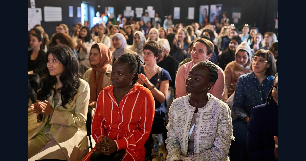 Participantes sentadas em um encontro da ReDI School Denmark, com outras pessoas ao fundo